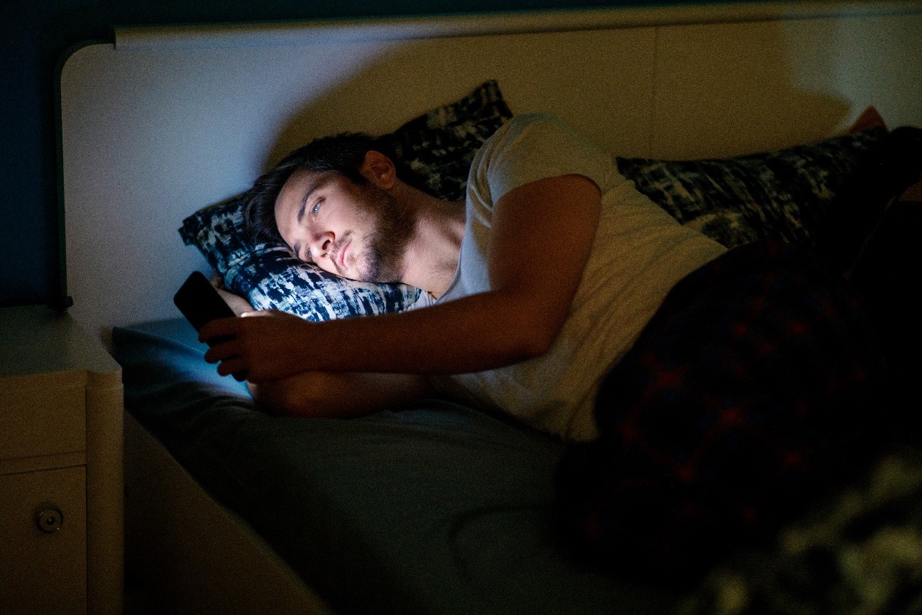 Homem deitado na cama, tudo escuro, com celular na mão