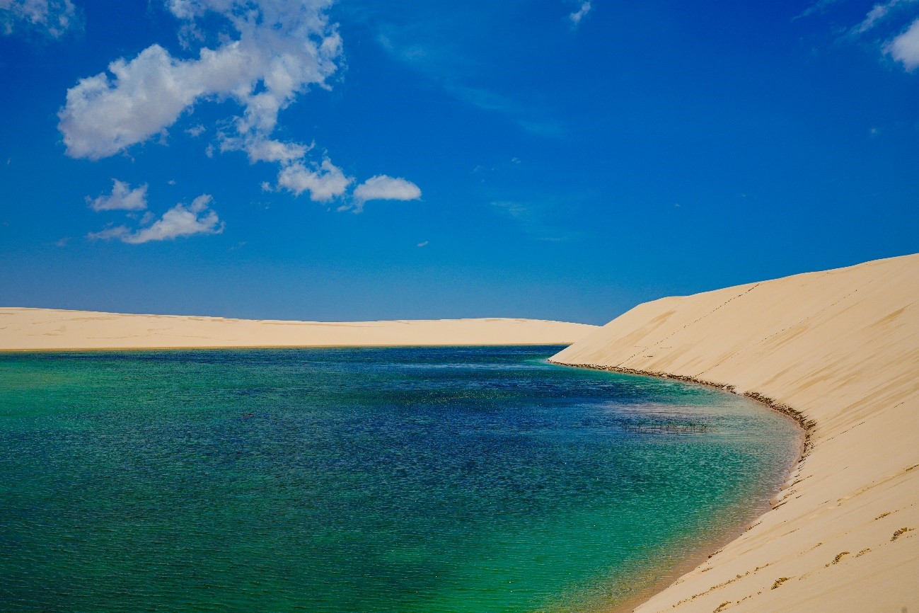 Imagem de uma lagoa cercada de areia branca nos Lençóis Maranhenses