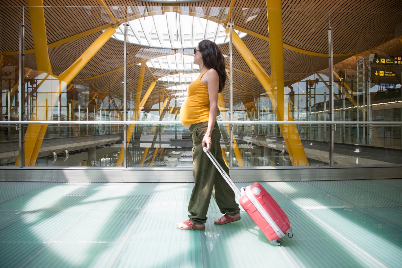 Gestante caminhando pelo aeroporto com uma bagagem de mão